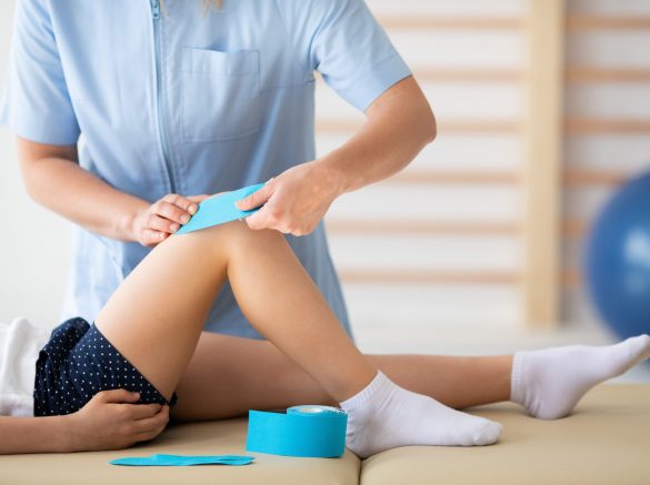 Close-up of physiotherapist taping girl's knee during physical therapy